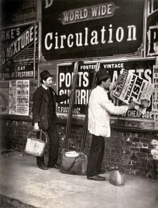 看板の上から広告を貼る2人の男性の白黒写真